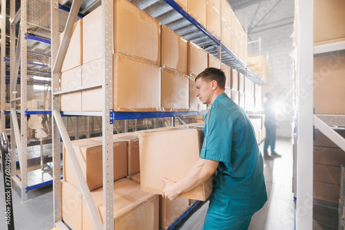 Warehouse worker in blue uniform holding package on shoulder for delivery to customer. Storage of medical products in med industry factory
