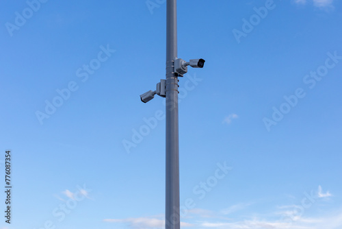 Two street surveillance cameras on pole against a blue sky background .Cameras are facing in opposite directions, full view. Security, surveillance, control concept