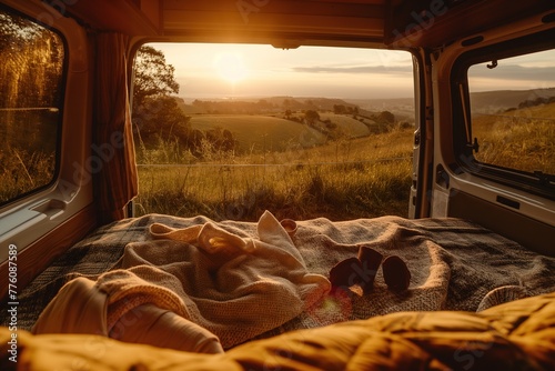 Sunset view from inside campervan, with bed and blanket overlooking hills in golden hour light. The landscape is serene and picturesque, creating an atmosphere of peaceful solitude.
