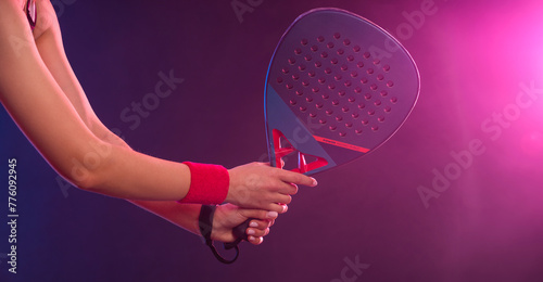 Close-up photo of Padel tennis player with racket on tournament. Girl athlete with paddle racket on court with neon colors. Download a high quality photo for design of a sports app or tour events. © Mike Orlov