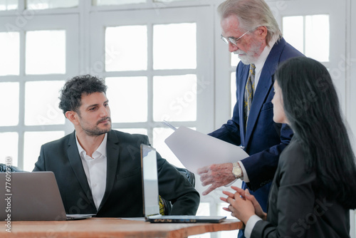 Multigenerational business team engaged in active discussion with a woman taking notes and a man on a call. A collaborative team of professionals in a meeting with one woman writing.