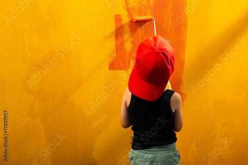 A boy on a yellow background draws with a red roller photo