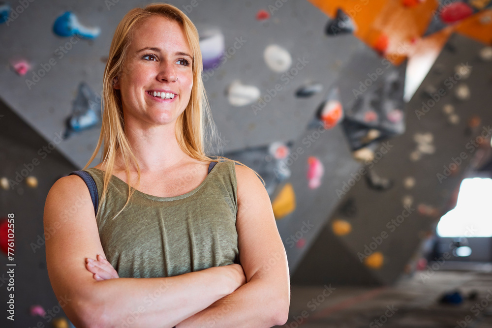 Fototapeta premium Portrait Of Female Coach In Front Of Climbing Wall At Indoor Centre With Climber In Background