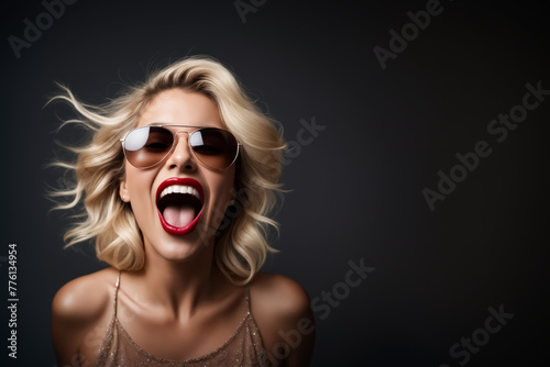 A woman with blonde hair and red lipstick is smiling and wearing sunglasses. She is wearing a gold dress and she is happy