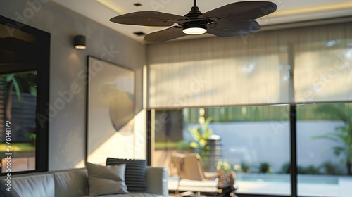 a living room.the rolling shade in the back of it in a insteresting way. the ceiling fan in the foreground, and the window with a smar roller shade in the background.