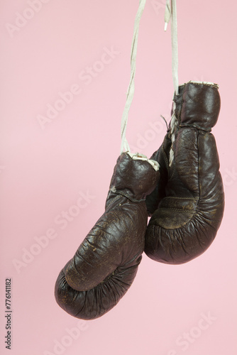 a pair of old boxing gloves hung in front of a candy-pink background