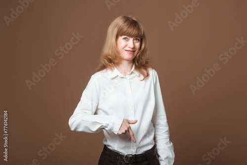 Portrait of Happy Middle-Aged Woman with Blonde Hair pointing fingers down, showing advertisement, recommending click on link, looking at camera, standing against beige background © AstiMak