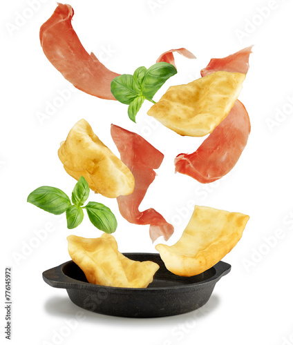 Deep fried dough, dry cured ham and basil leaves falling into  a cast iron pan isolated on white. Italian antipasto ingredients.