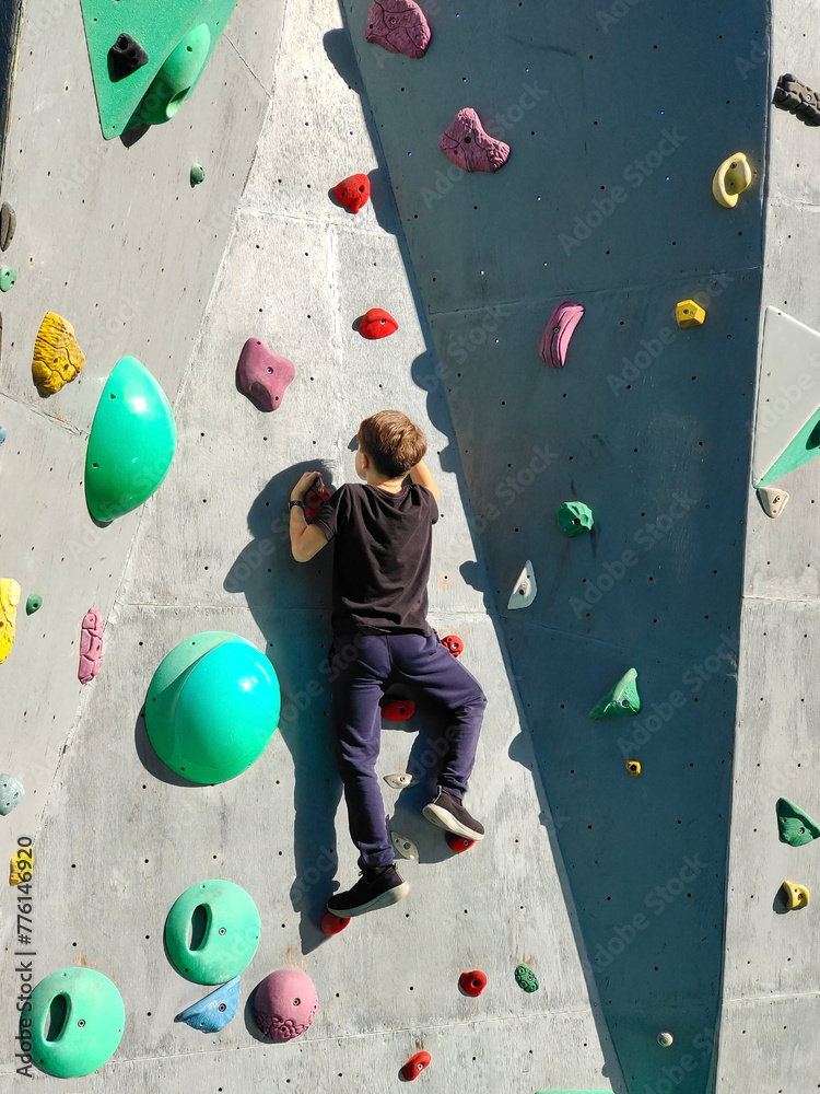 Fototapeta premium A teenage boy is exercising and climbing a rock-climbing wall. An example of the active sports life of young people