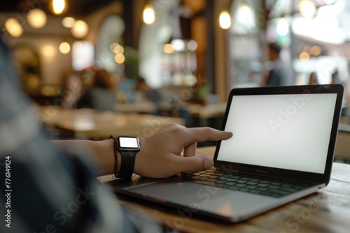 A hand with a smartwatch mockup screen typing on a laptop in a coffee shop photo