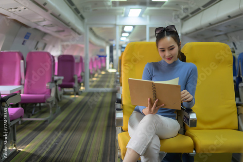A woman is reading a book on a yellow seat in an airplane
