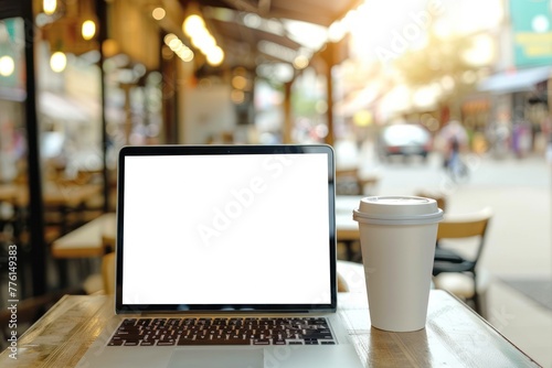 A person holds a coffee cup in a cafe, typing on a laptop with white mockup screen
