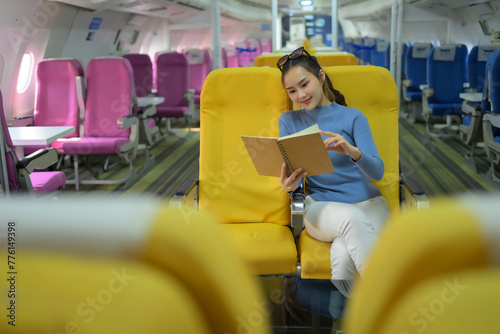 A woman is sitting on a yellow seat reading a book