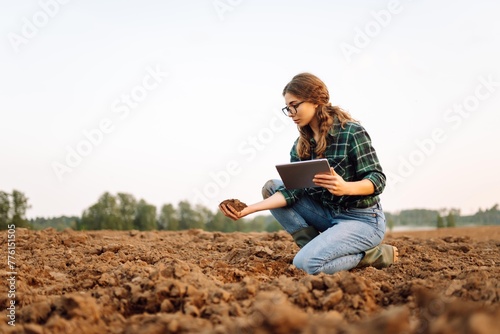 Farmer woman with a digital tablet holds black soil in her hands and checks the quality. Concept of technology, ecology and gardening. © maxbelchenko