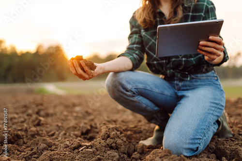 Farmer woman with a digital tablet holds black soil in her hands and checks the quality. Concept of technology, ecology and gardening.