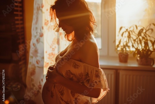 pregnant young woman with belly in front of sunny window photo