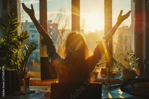 Silhouette of super happy woman sitting at desk with arms raised up in front of sunny window