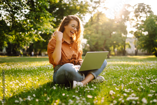 Young curly woman in the park with laptop on the green grass. Education online. IT. Business, blogging, freelance concept. © maxbelchenko