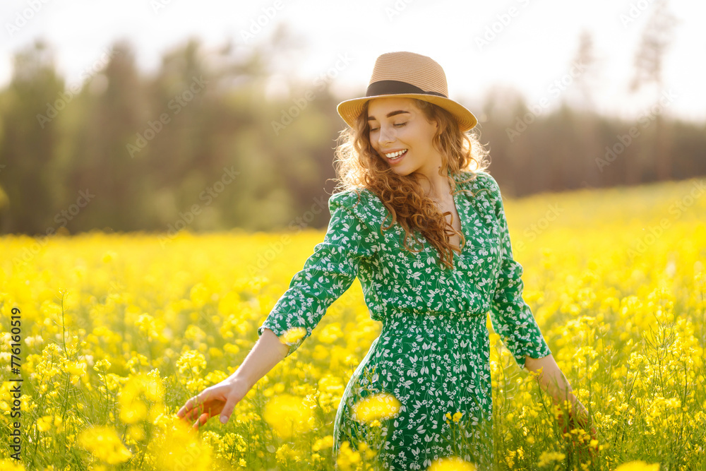 Fototapeta premium Beautiful woman walking in the field at sunny summer day. Nature, vacation, relax and lifestyle. View scenic landscape yellow flower blooming.