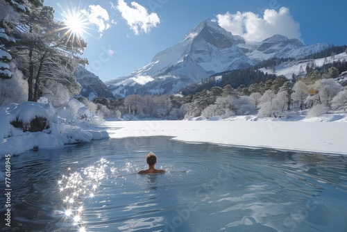 A brave individual takes a winter swim in a freezing lake with a stunning snowy mountain background under the clear blue sky