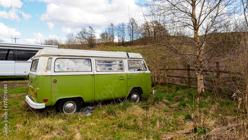 Old classic green painted camper van with white pop top left in a field