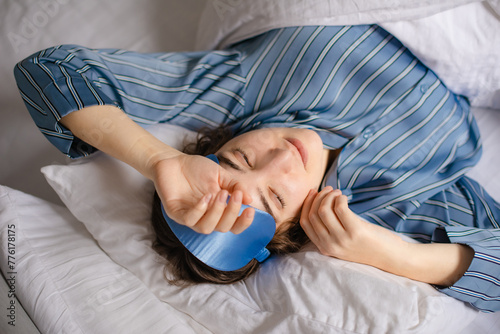 woman removes silk sleeping mask from her eyes in morning