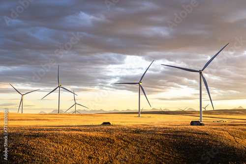 Row of windmills generating electricity on the Canadian prairies overlooking a pair on old farm sheds under a dramatic sunset sky near Pincher Creek Alberta. photo