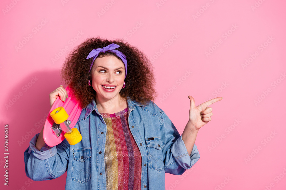 Photo of cool cheerful lady dressed jeans outfit holding skate board pointing emtpy space isolated pink color background