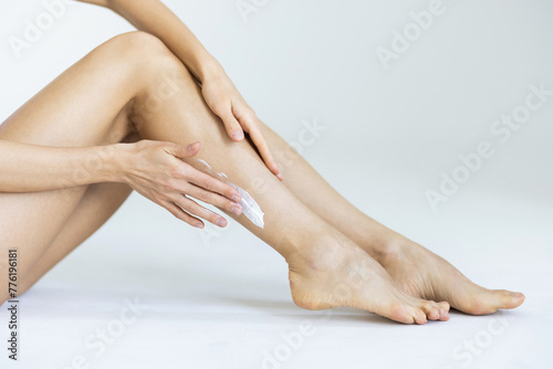 Young woman applying body cream onto her smooth legs on light grey background, closeup © F8  \ Suport Ukraine