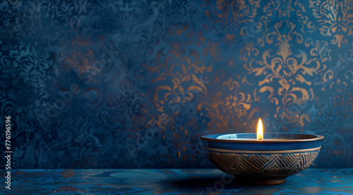 A single lit candle in an elegant, decorative bowl against the backdrop of intricate blue wallpaper with soft lighting and copy space for text