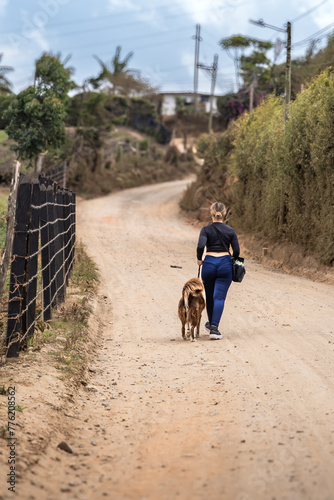 Young adult woman walking with her border collie dog on rural road in Colombia