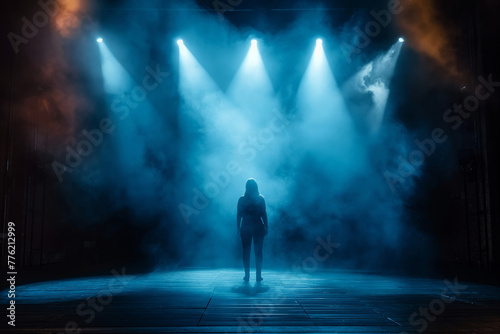A dramatic image of a lone figure standing under intense blue stage lights with atmospheric fog and a sense of anticipation © StockUp