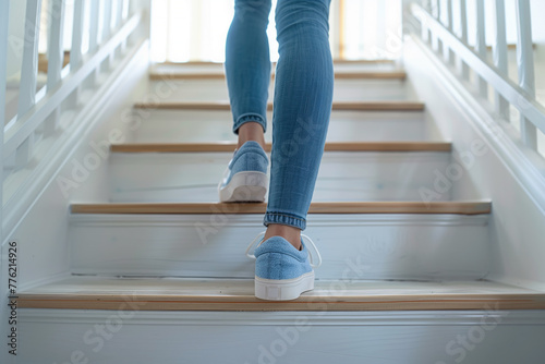 Woman walking up a white wooden staircase, casual sneakers in focus. Close-up on female feet in blue denim jeans and light blue shoes ascending steps, concept of movement and everyday lifestyle
