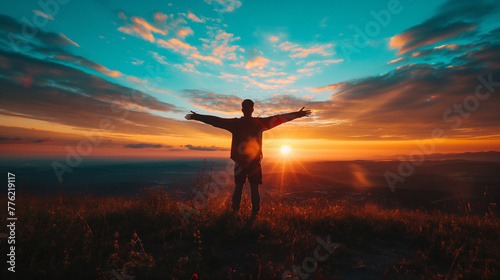 A man stands on a hilltop watching the sunrise, silhouetted against the light of a new day, his hands wide open, embracing hope and possibility photo