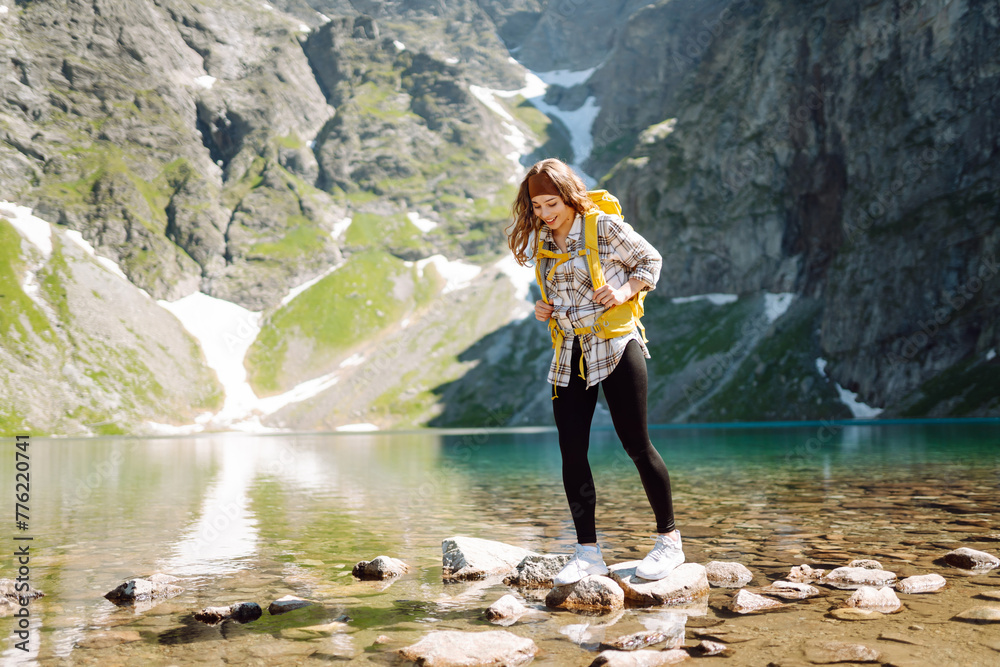 Young woman with a yellow hiking backpack traveling along hiking trails in the mountains among forests and cliffs.  Lifestyle, adventure, nature, active life.