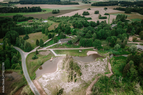 Valmiera, Latvia - Augist 13, 2023 - An aerial view of a rural landscape with a building, a curved pond with a pier, surrounding greenery, and cultivated fields in the background... photo