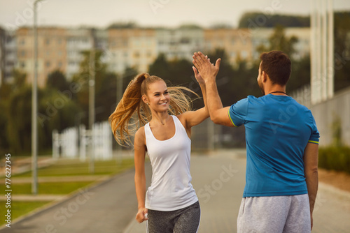 Woman gives a high five to man coach during a workout session in the city park. This portrait embodies the dynamic connection between trainer and trainee in the pursuit of fitness goals.