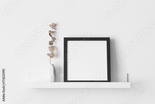 Black square frame mockup with an eucalyptus decoration on the wall shelf.