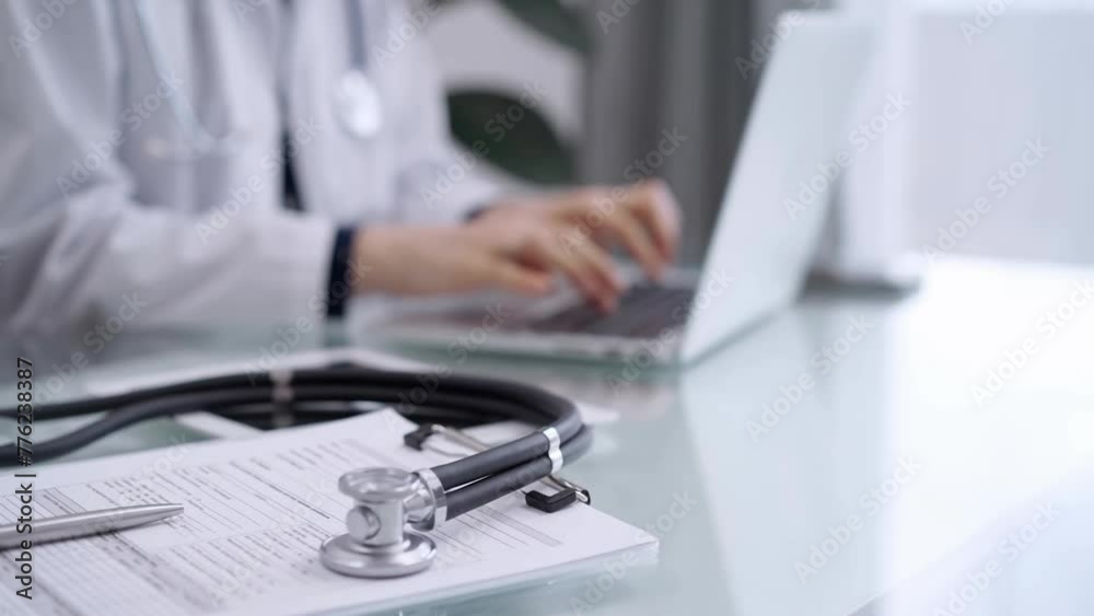 Stethoscope and medical clipboard are lying on the glass table while doctor woman is working with laptop computer on the background. Medicine and pharmacy concept Stethoscope and medical clipboard are lying on the glass table while doctor woman is working with laptop computer on the background. Medicine and pharmacy concept