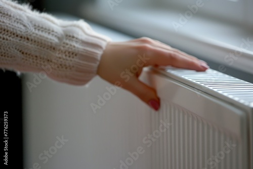 a woman in a jacket reaches out with her hand to the radiator switch in a bright room to save electricity.