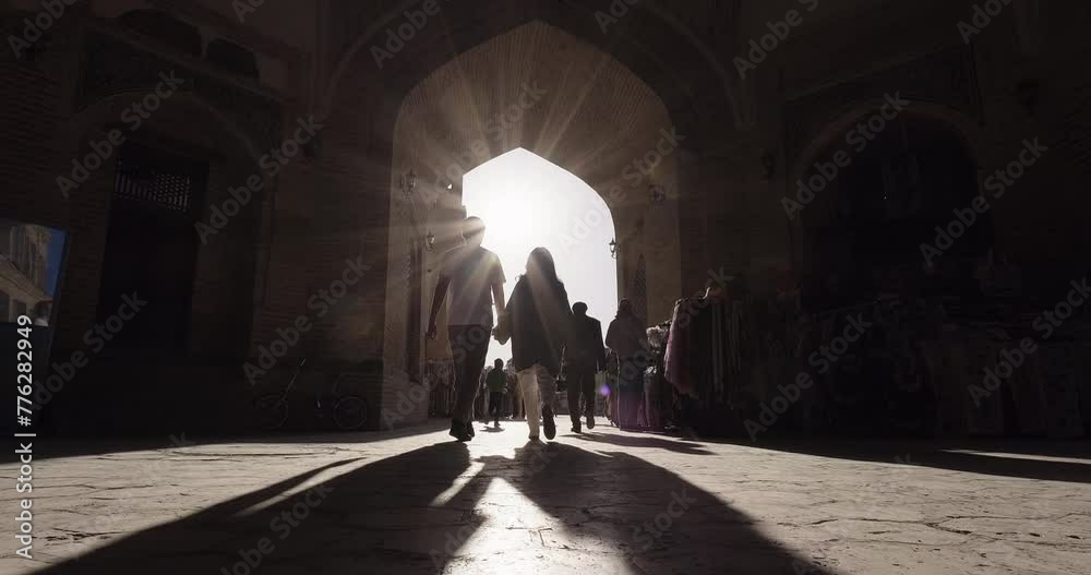 Young couple walking together through ancient streets of Bukhara, Uzbekistan. Silhouette of romantic couple in love against sunlight. Travel, romantic trip, happiness, love, connection, relationship