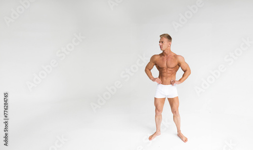 tanned male bodybuilder in white shorts against a white wall in the studio, sexy blond man