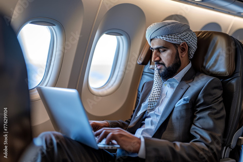 A man in a suit is working on a laptop while sitting in an airplane seat