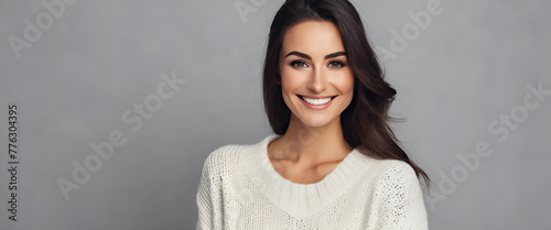 A beautiful woman with long dark hair and brown eyes, wearing an elegant white sweater with turtleneck, smiling at the camera in front of a grey background