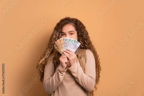 fun female student with money, brazilian real in beige studio background. finance, investment, offer, loan concept. 