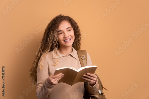 joyful caucasian woman reading book to study in beige studio background. going to school, education, student concept.