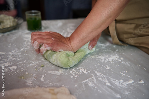 Close-up hands of a housewife kneading dough on the floured kitchen table, making dumplings for dinner