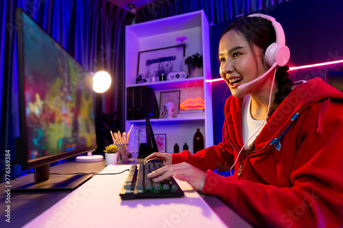 Host channel of young beautiful Asian gaming streamer playing fighting Moba at battle arena game on pc screen with multiplays, wearing pastel headphone at neon digital light modern room. Stratagem. photo