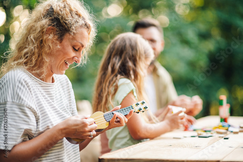 Side view of a happy mother playing ukulele toy in nature to her family