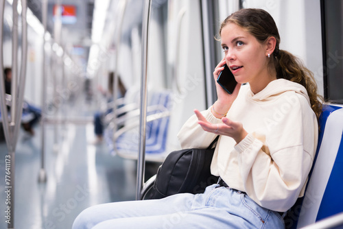 Portrait of an active positive girl talking on a mobile phone on a subway train photo